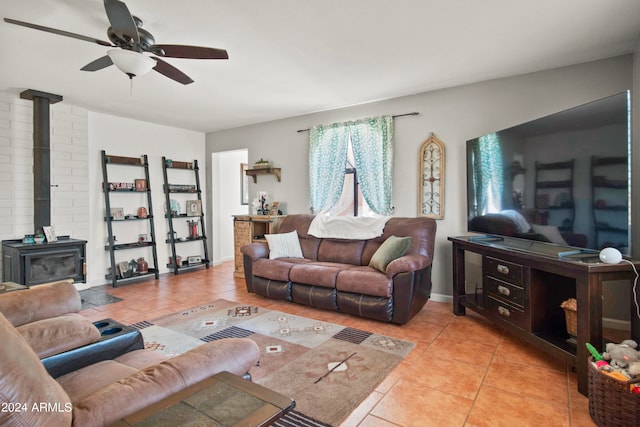 living room featuring ceiling fan, a wood stove, and light tile patterned floors