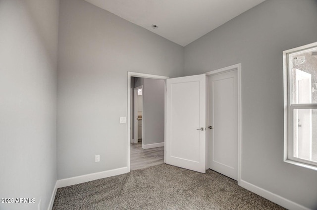 unfurnished bedroom featuring lofted ceiling, carpet flooring, and baseboards