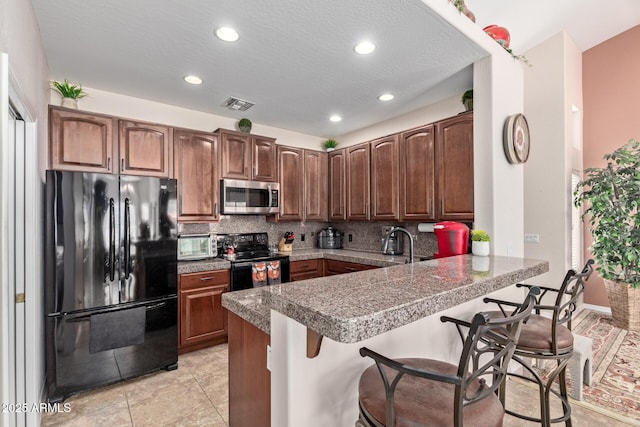 kitchen featuring black appliances, kitchen peninsula, decorative backsplash, and a kitchen breakfast bar