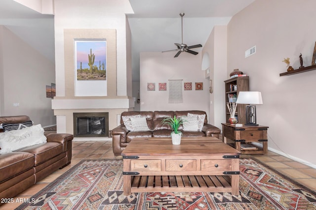 tiled living area featuring a fireplace, visible vents, a high ceiling, a ceiling fan, and baseboards