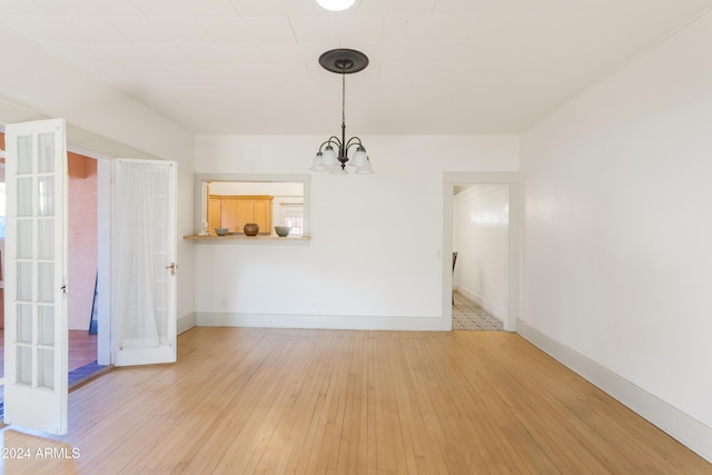 unfurnished dining area featuring hardwood / wood-style floors, a notable chandelier, french doors, and baseboards