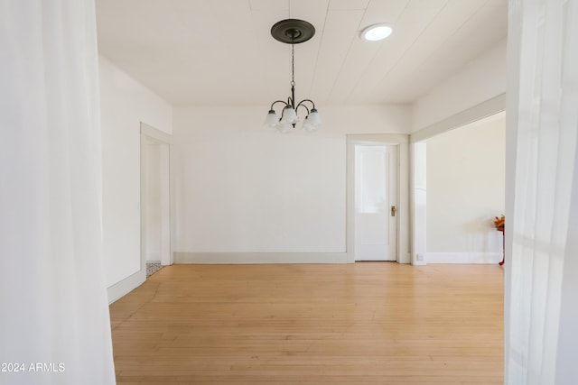 unfurnished dining area featuring baseboards, a notable chandelier, and light wood finished floors