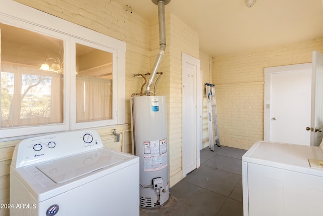 washroom featuring laundry area, dark tile patterned floors, water heater, and brick wall