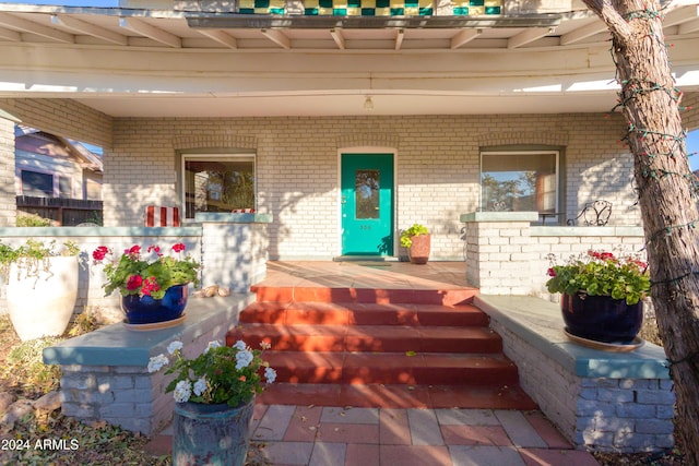 doorway to property with brick siding and a porch