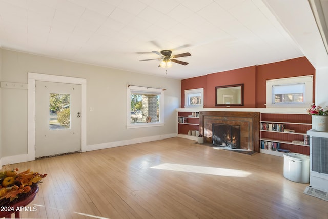 living area with baseboards, a ceiling fan, a lit fireplace, and wood-type flooring