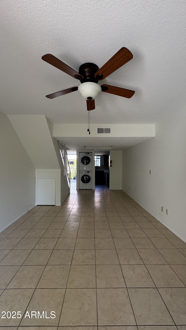 unfurnished living room featuring visible vents, a textured ceiling, light tile patterned flooring, and stacked washer / dryer