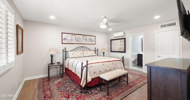 bedroom with a wall mounted AC, dark hardwood / wood-style flooring, ensuite bathroom, and ceiling fan