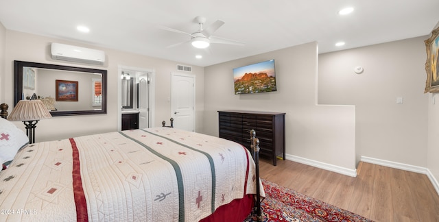 bedroom with ceiling fan, ensuite bathroom, a wall mounted air conditioner, and light hardwood / wood-style flooring