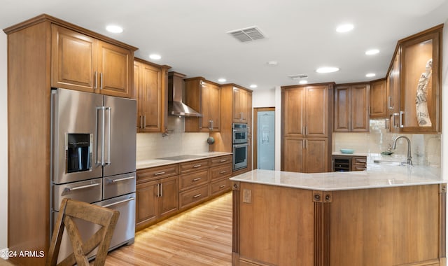 kitchen featuring stainless steel appliances, light hardwood / wood-style floors, sink, wall chimney range hood, and kitchen peninsula