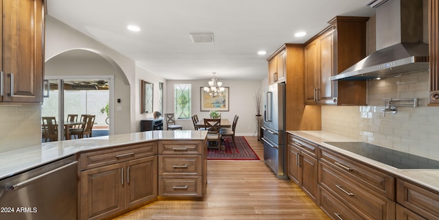 kitchen featuring an inviting chandelier, pendant lighting, light hardwood / wood-style floors, stainless steel appliances, and wall chimney range hood