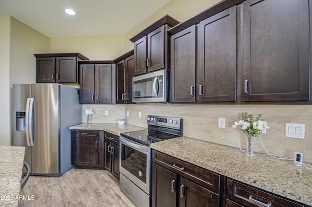 kitchen with dark brown cabinetry, light wood finished floors, decorative backsplash, light stone counters, and stainless steel appliances