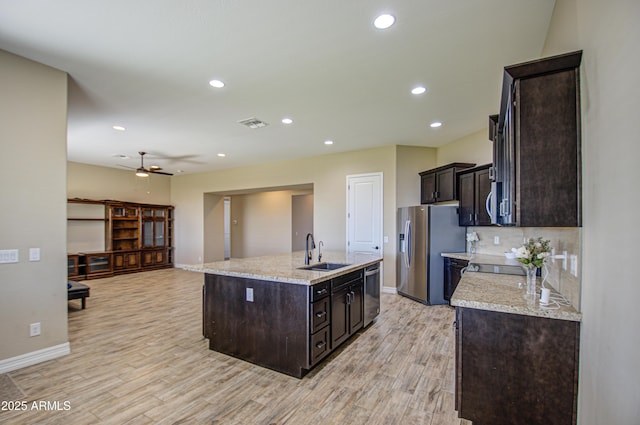 kitchen featuring a kitchen island with sink, stainless steel appliances, a sink, light wood-style floors, and dark brown cabinets