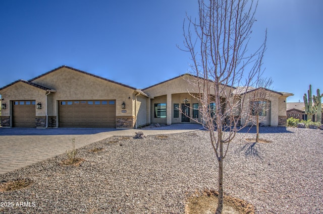 single story home featuring an attached garage, stone siding, decorative driveway, and stucco siding