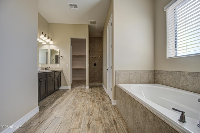 bathroom with vanity, wood finished floors, a garden tub, and visible vents