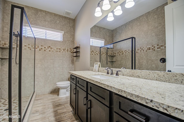 full bathroom with toilet, visible vents, tiled shower, and vanity