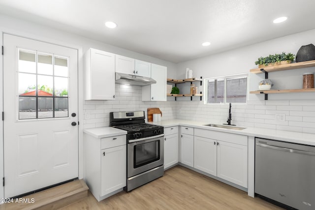 kitchen with appliances with stainless steel finishes, sink, white cabinets, decorative backsplash, and light hardwood / wood-style flooring