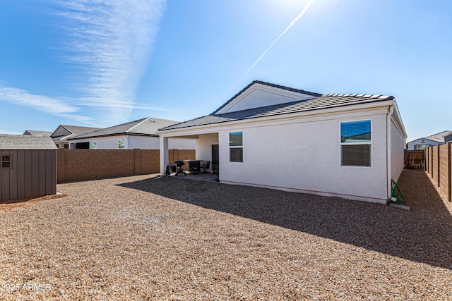 back of house with a fenced backyard, an outdoor structure, a patio area, a shed, and stucco siding