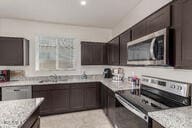 kitchen featuring dark brown cabinetry, light stone counters, stainless steel appliances, and a sink