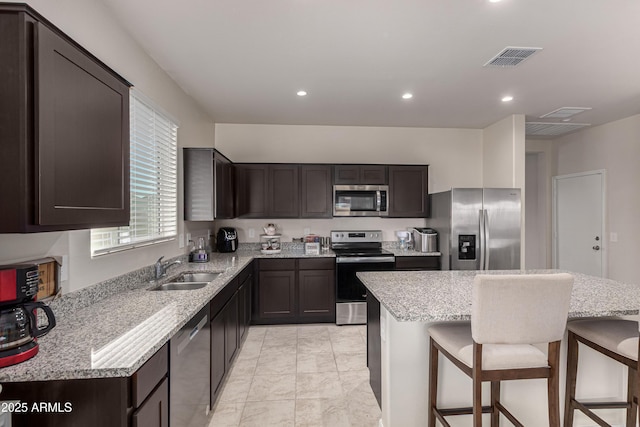 kitchen featuring visible vents, appliances with stainless steel finishes, dark brown cabinetry, a sink, and a kitchen bar