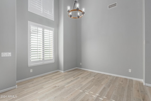 spare room with a notable chandelier and light wood-type flooring