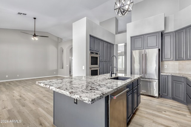 kitchen featuring appliances with stainless steel finishes, vaulted ceiling, a kitchen island with sink, sink, and gray cabinets