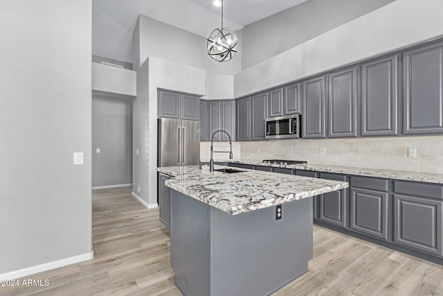 kitchen featuring gray cabinetry, sink, an island with sink, decorative light fixtures, and stainless steel appliances