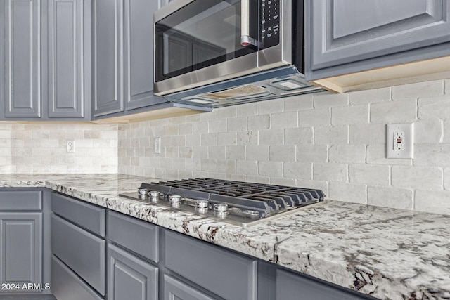 kitchen with gray cabinetry, decorative backsplash, light stone countertops, and appliances with stainless steel finishes