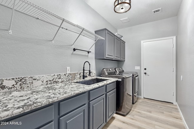 clothes washing area with separate washer and dryer, cabinets, sink, and light hardwood / wood-style floors