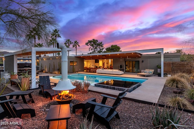 pool at dusk featuring an outdoor living space with a fire pit and a patio