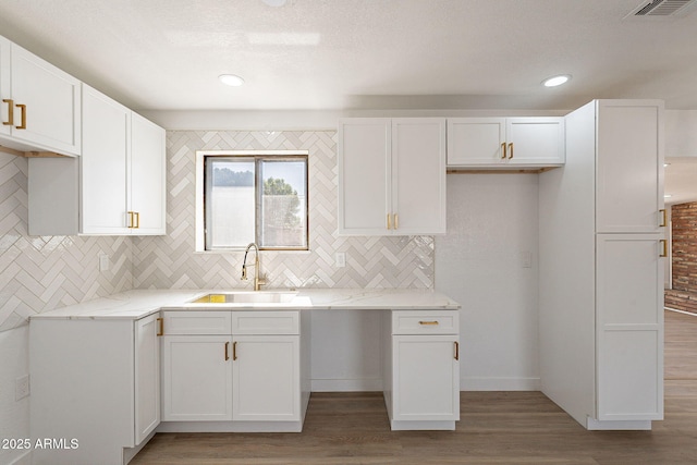 kitchen with light stone counters, wood finished floors, visible vents, a sink, and white cabinetry