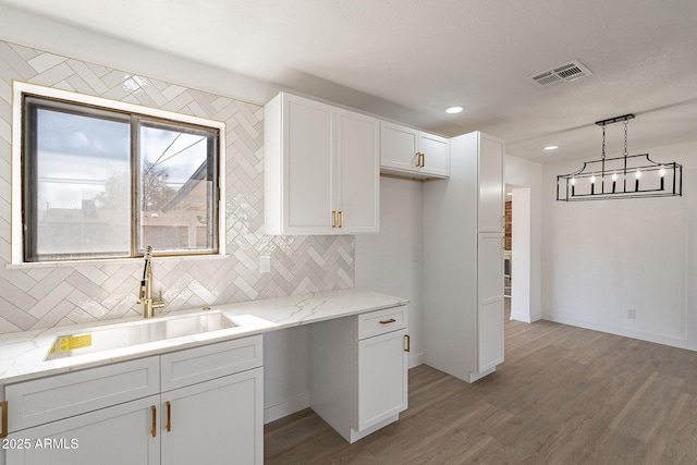 kitchen featuring visible vents, white cabinets, wood finished floors, decorative light fixtures, and a sink