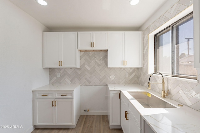 kitchen featuring tasteful backsplash, a sink, white cabinetry, and light stone countertops