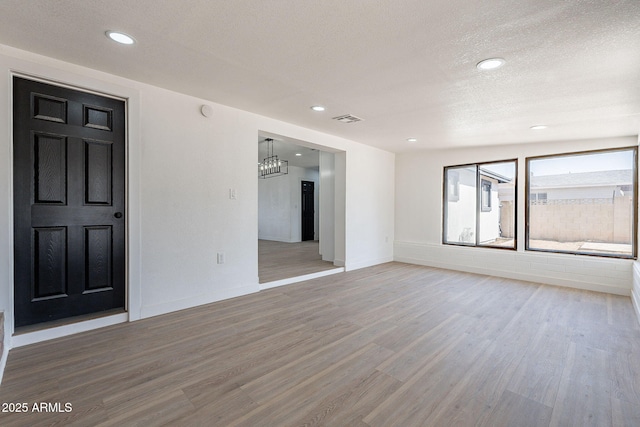 unfurnished room with a textured ceiling, wood finished floors, visible vents, and baseboards