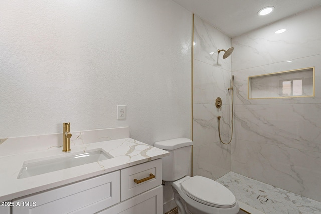 bathroom featuring toilet, a textured wall, a marble finish shower, and vanity