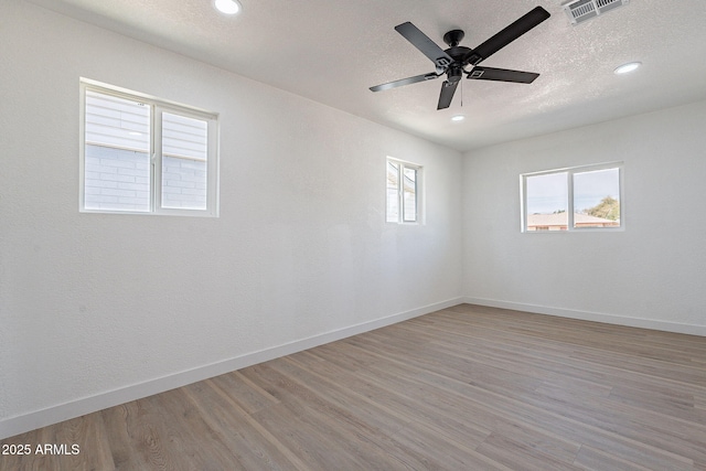 spare room featuring light wood-style floors, baseboards, visible vents, and a textured ceiling