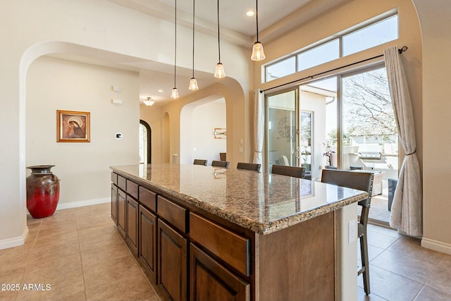 kitchen featuring light tile patterned floors, a breakfast bar, stone counters, and a center island