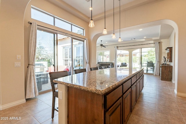 kitchen with baseboards, arched walkways, light stone counters, a center island, and pendant lighting