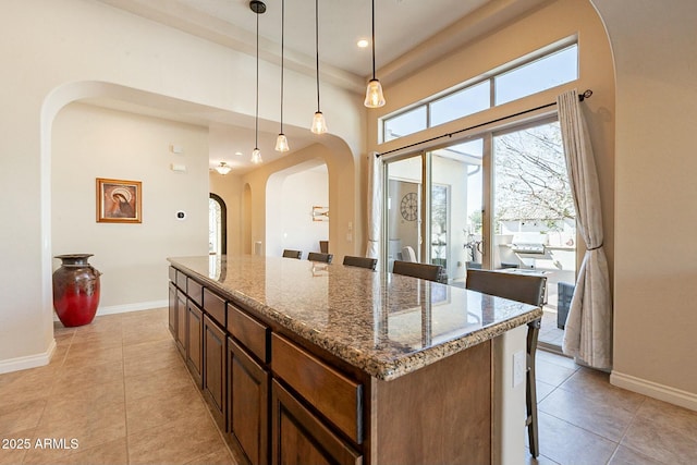 kitchen featuring baseboards, stone counters, light tile patterned flooring, and a center island