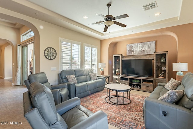 tiled living area with visible vents, arched walkways, a tray ceiling, and recessed lighting