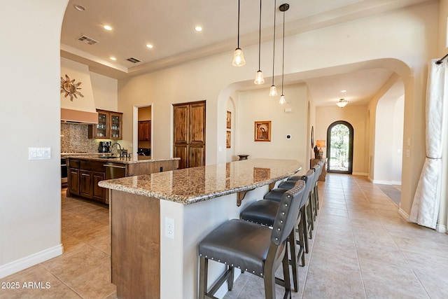 kitchen with visible vents, arched walkways, backsplash, and a large island with sink