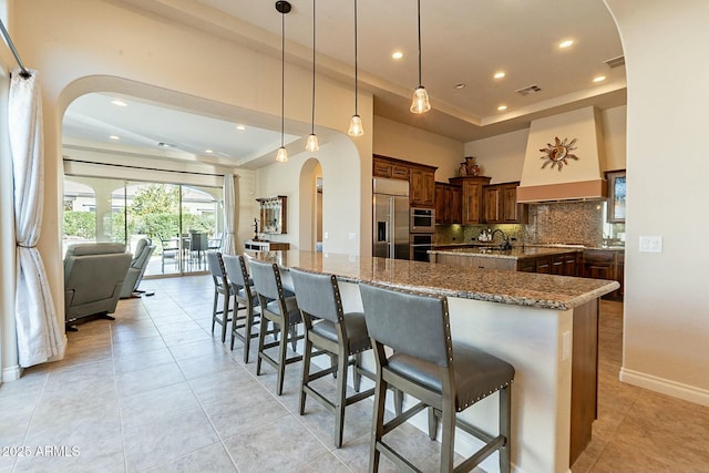 kitchen with arched walkways, stainless steel appliances, a tray ceiling, and a spacious island