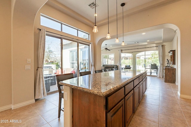 kitchen featuring light tile patterned floors, visible vents, arched walkways, a center island, and light stone countertops