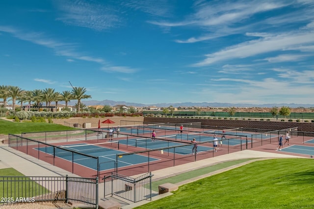 view of tennis court featuring fence, a mountain view, and a lawn