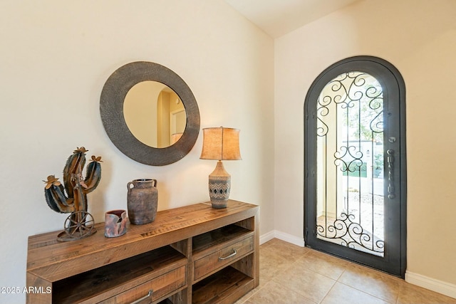 entryway featuring arched walkways, light tile patterned flooring, lofted ceiling, and baseboards