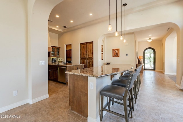 kitchen featuring arched walkways, dishwasher, a large island, and a sink