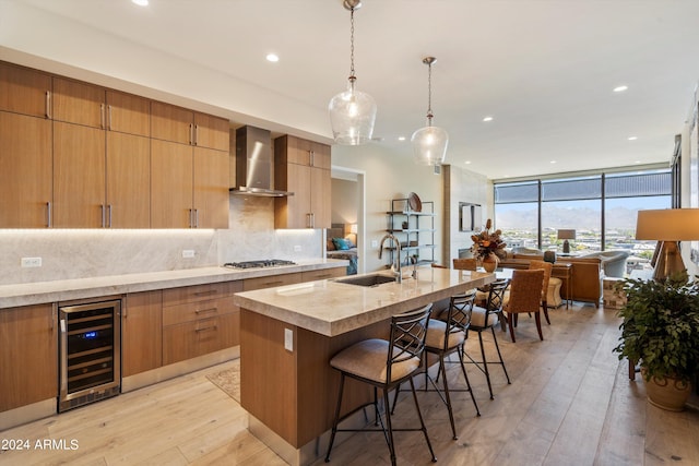 kitchen with wine cooler, tasteful backsplash, a kitchen island with sink, sink, and wall chimney range hood