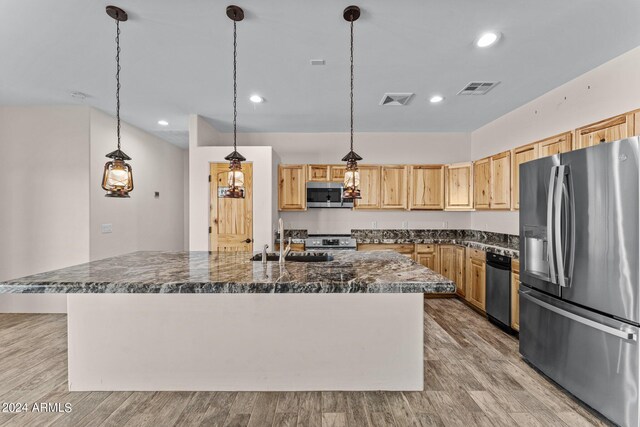 kitchen with a kitchen island with sink, hanging light fixtures, stainless steel appliances, and light hardwood / wood-style floors