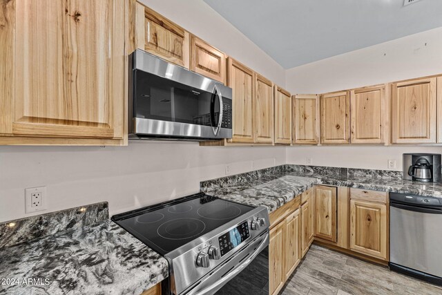 kitchen with dark stone counters, light hardwood / wood-style floors, appliances with stainless steel finishes, and light brown cabinetry