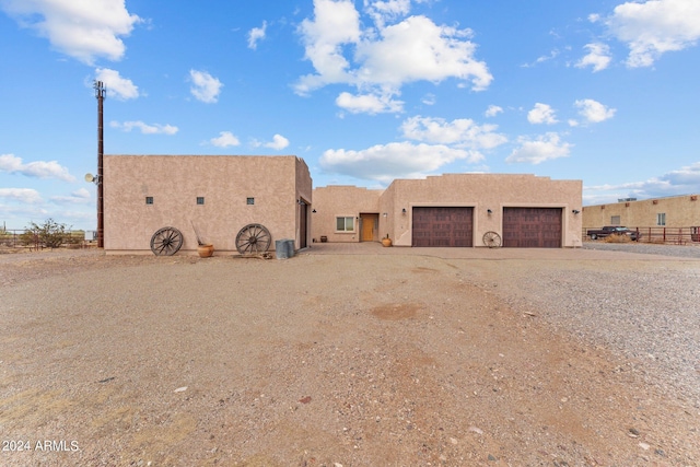 pueblo-style home featuring a garage, driveway, fence, and stucco siding