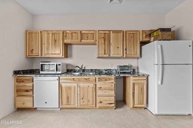 kitchen with sink, dark stone countertops, light tile patterned floors, and white appliances